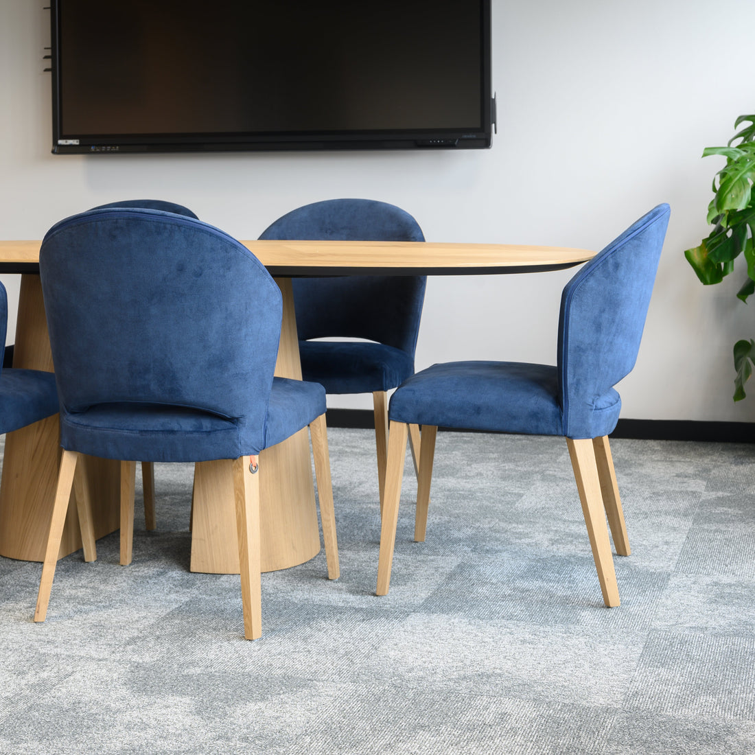 Conference/Meeting room with blue chairs around a extendable wooden table and a TV on the wall.