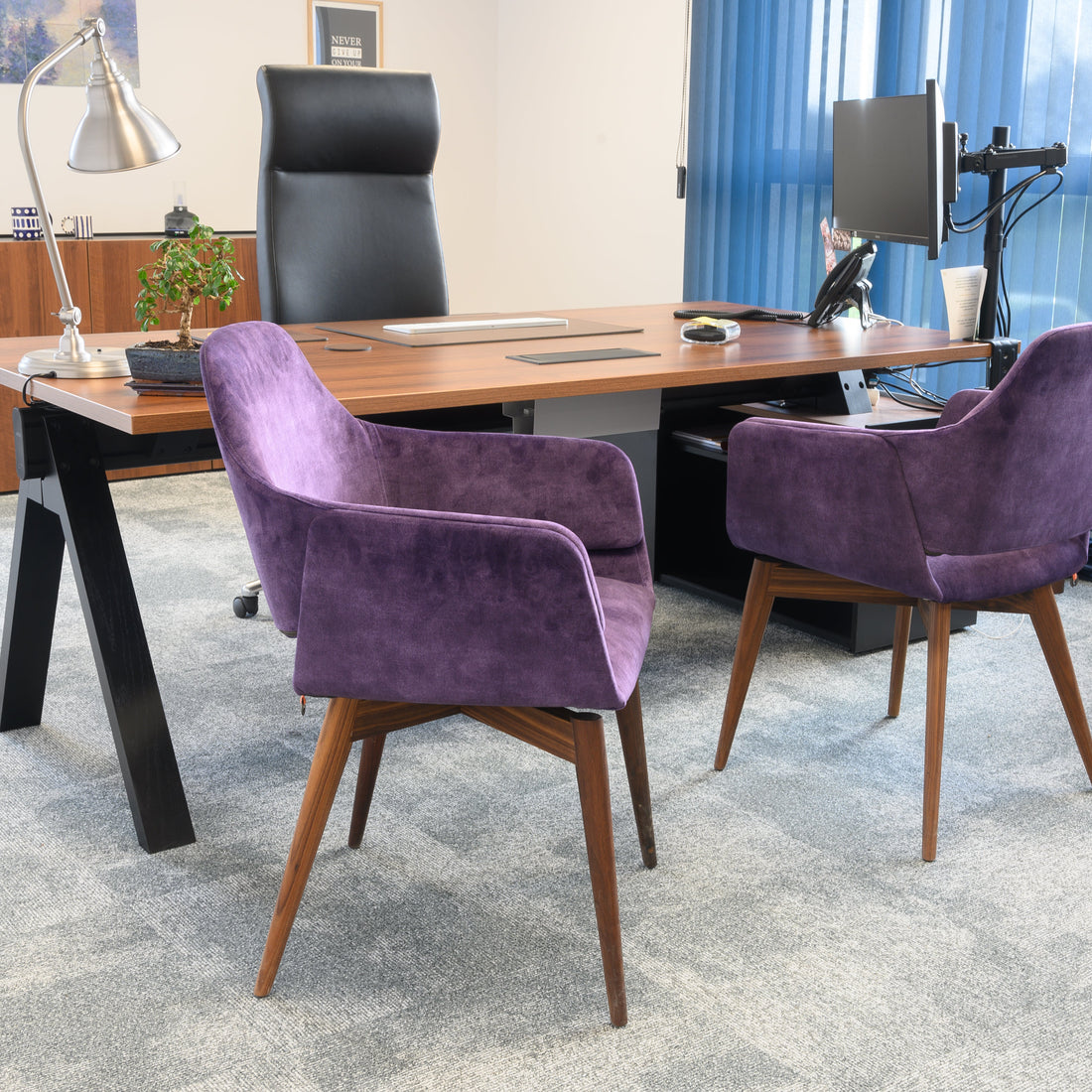 Modern office setup with a wooden desk, black leather ergonomic chair, and purple armchairs.