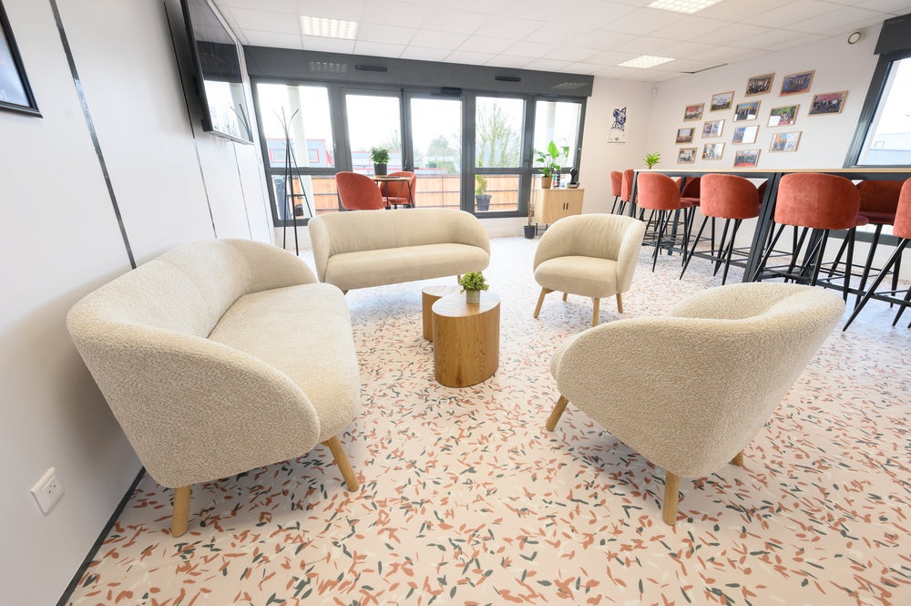 Modern office break area with beige armchairs and a small wooden coffee table. High terracotta red bar stools and wooden tables. 
