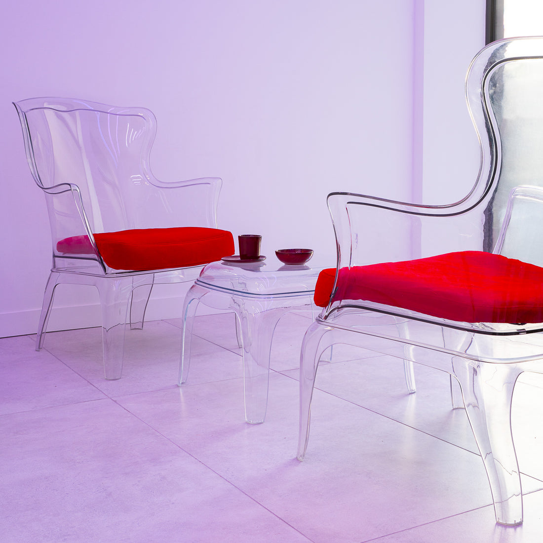Clear chairs with red cushions on a white floor and light purple wall