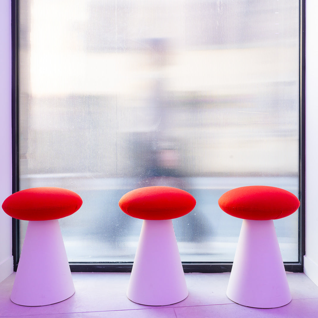 Three red and white stools in front of a large window with a blurred view.