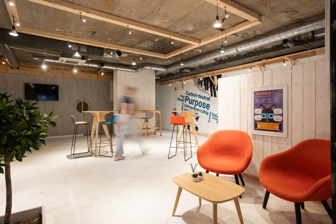 Modern communal zone in office space with orange chairs, wooden tables, and motivational posters on a white wall.