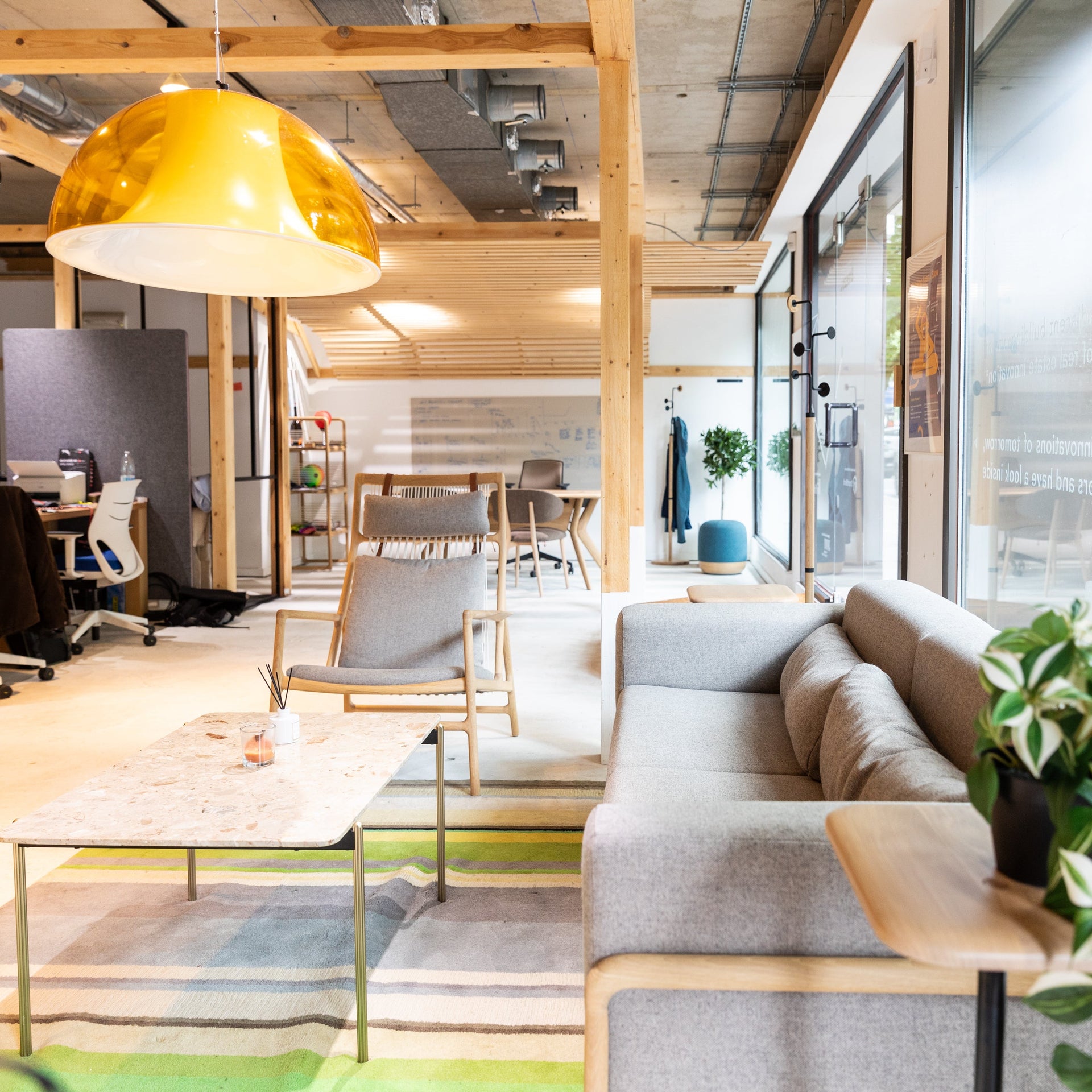 Modern office interior with a gray sofa, coffee table, and yellow pendant light.