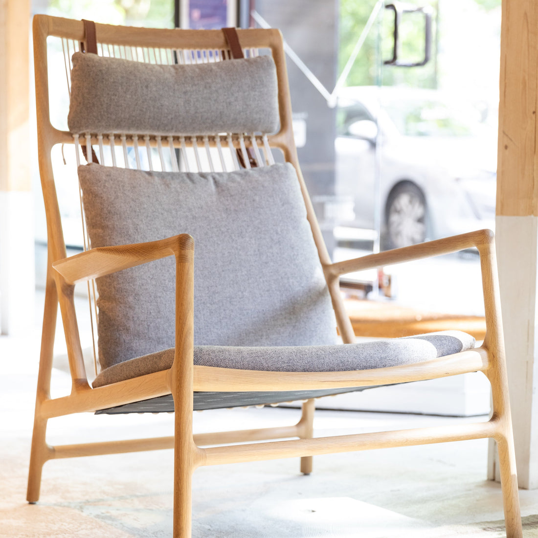 Wooden chair with gray cushions in a bright room with large windows.