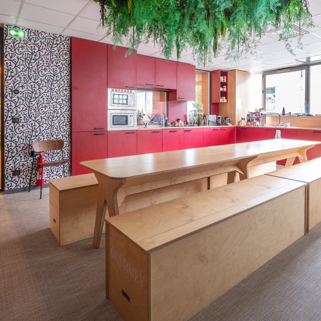Modern kitchen with red cabinets, wooden island, and green plants.