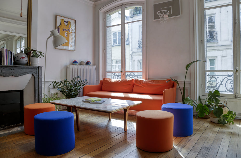 Office break out area with orange sofa, blue ottomans, marble top coffee table, and large windows.