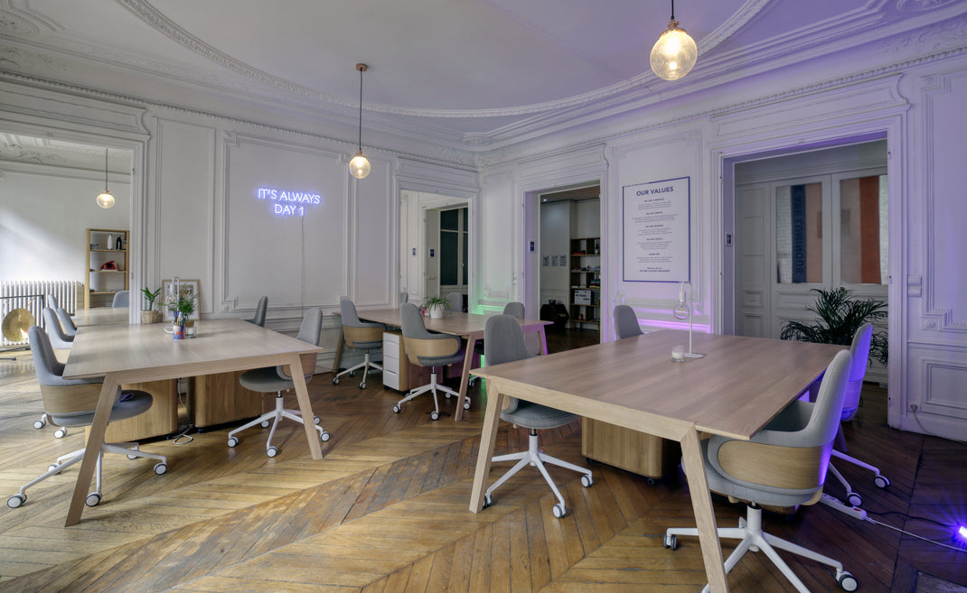 Modern office space with wooden tables and chairs, white walls, and decorative elements.