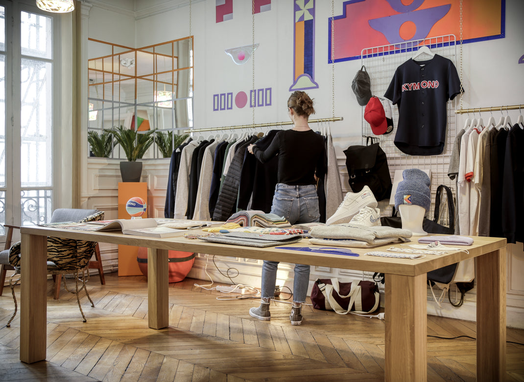 Person standing near a table with clothing items in a room with artistic wall decorations.