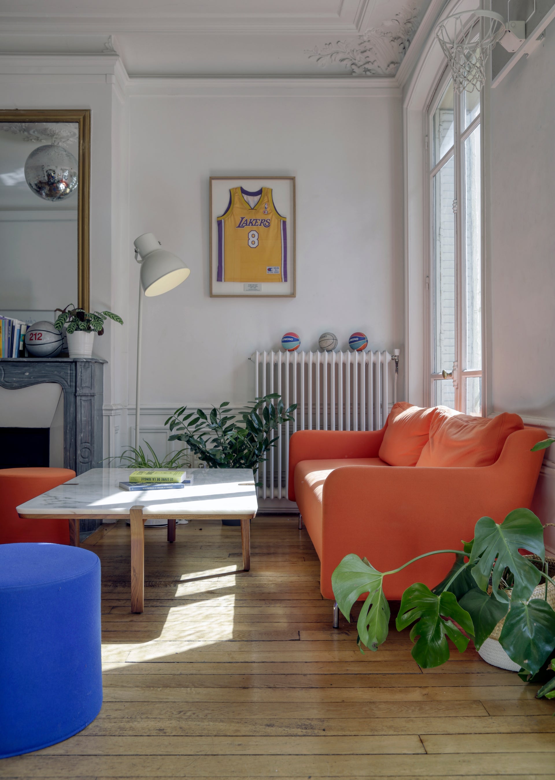 Office break out area with orange sofa, blue ottoman, and framed sports jersey on wall.