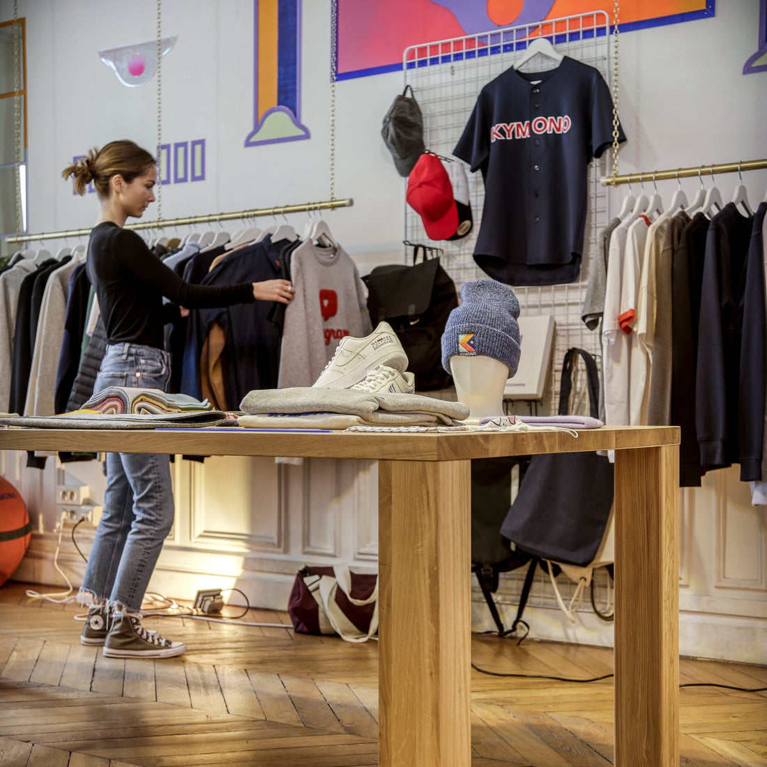Person in a store looking at jumpers, shoes on a table with racks of clothes in the background