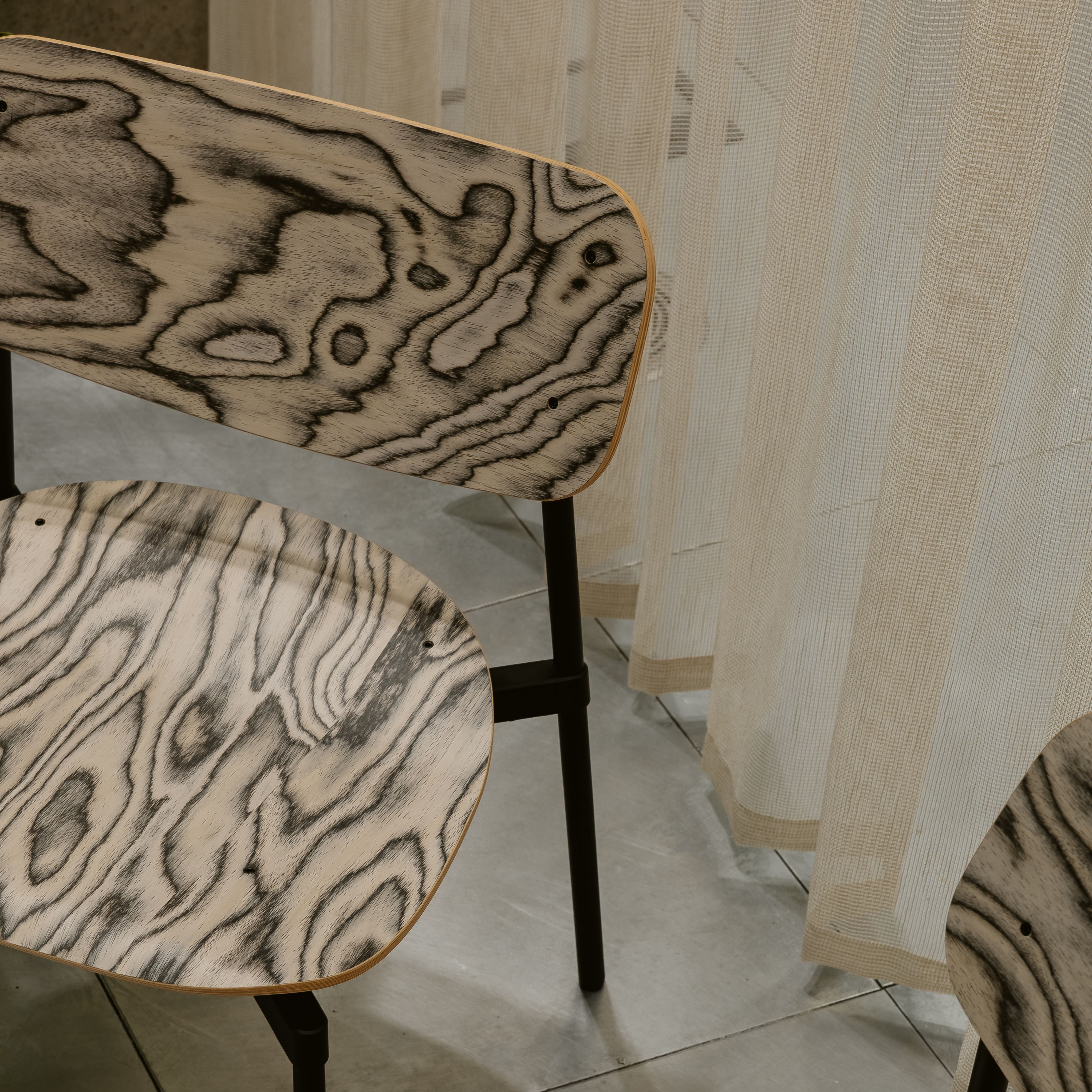 Three chairs with wood-patterned seats and backs in a room with tiled floor and striped wallpaper.