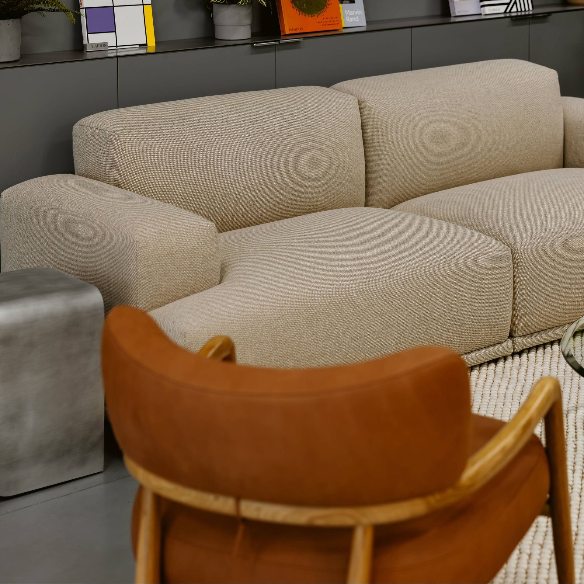 Beige sectional sofa in a modern living room with a brown chair and glass coffee table.