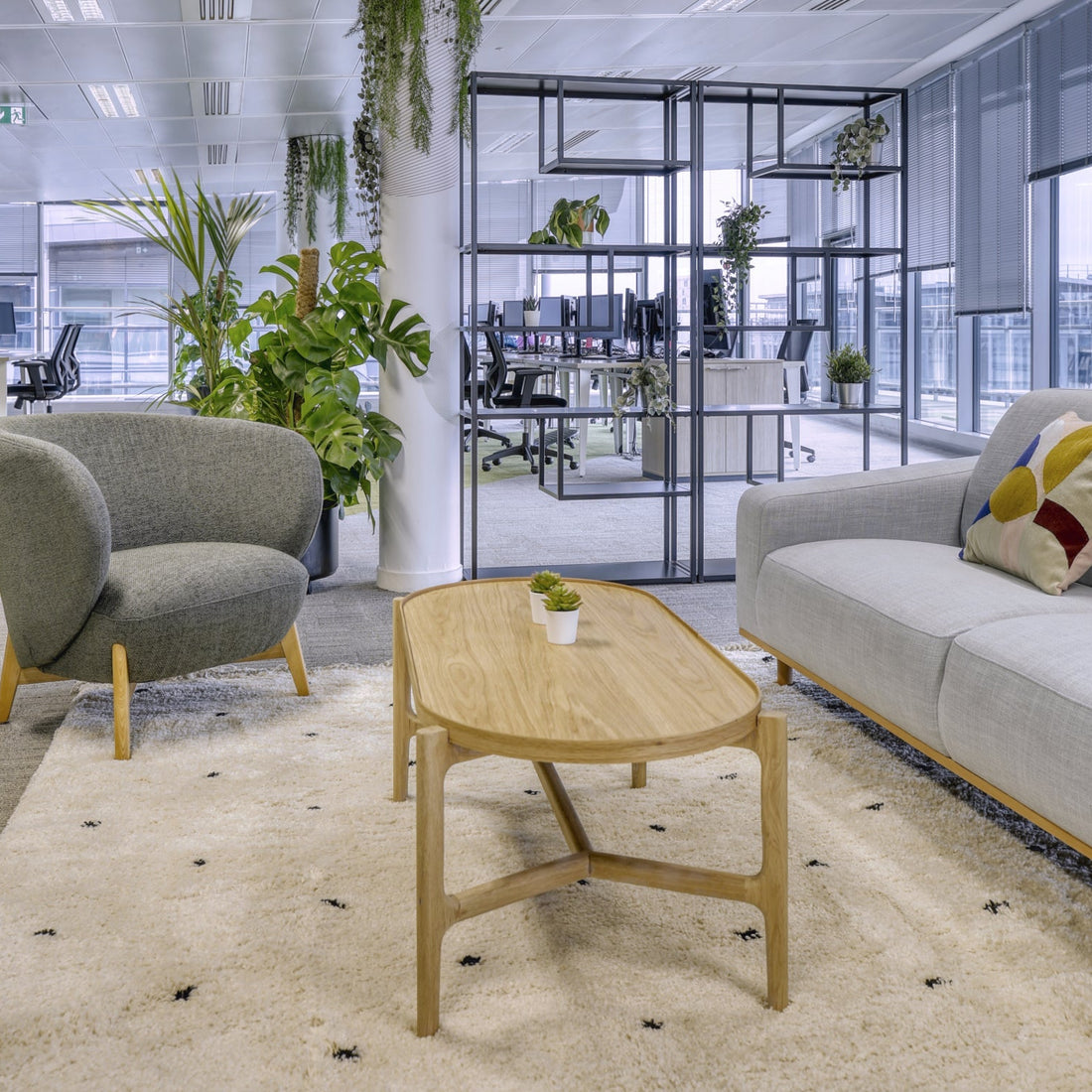 Modern office lounge with gray sofa, armchair, and wooden coffee table.