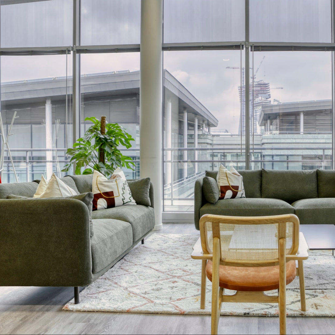 Modern living room with green sofas, wooden chairs, and large windows.