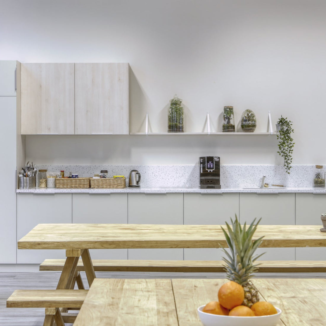 Modern kitchen with wooden dining table and bench, plants, and kitchen appliances.