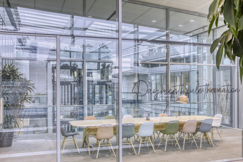 Modern office conference room with glass walls and a long table with colourful chairs.