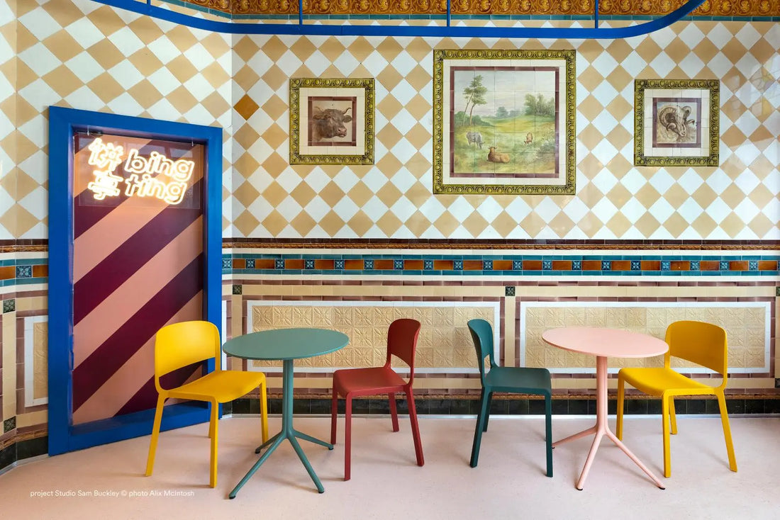 Colorful chairs and tables arranged in a room with patterned walls and framed pictures.