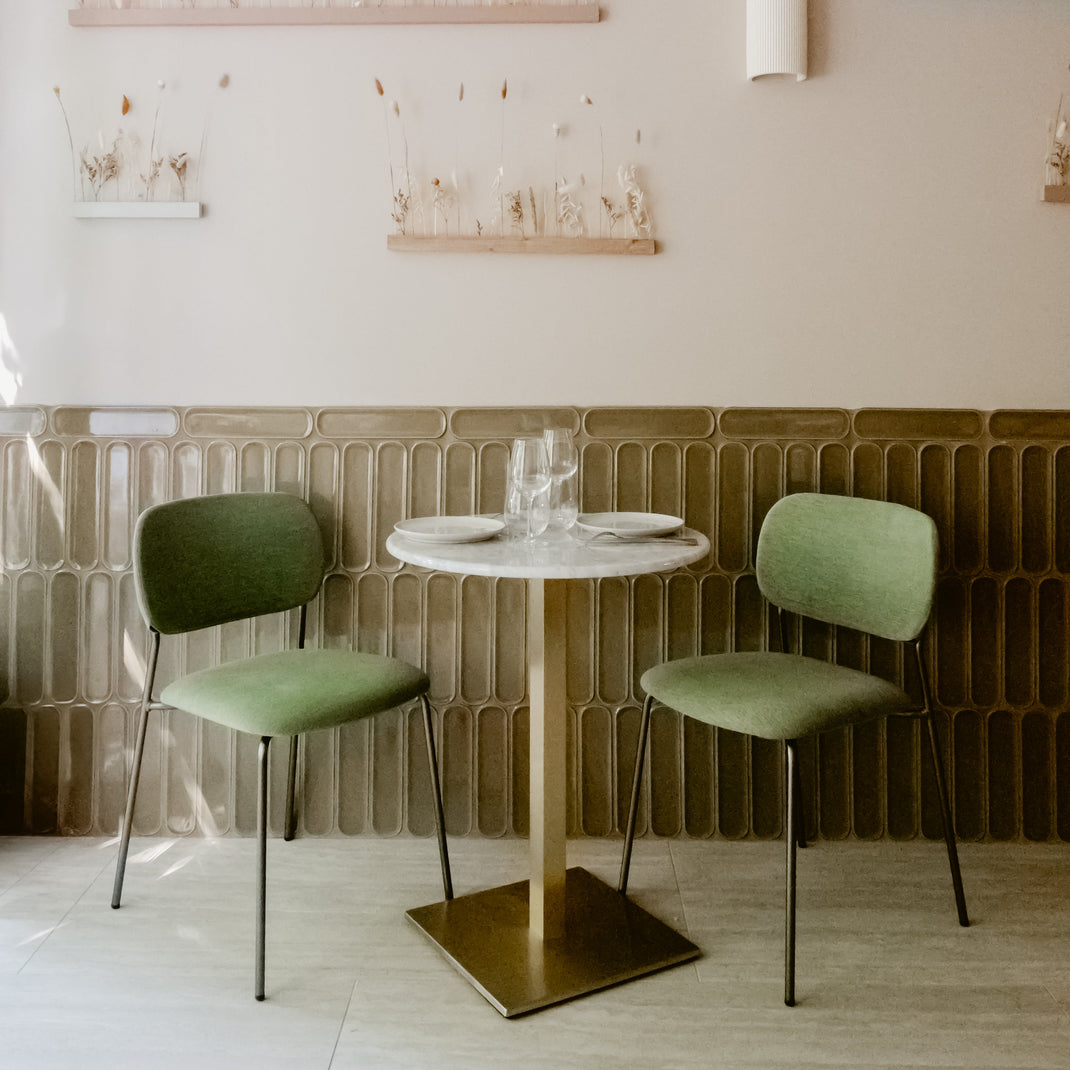 restaurant/café with green fabric covered seating and round marble table with brass leg. 