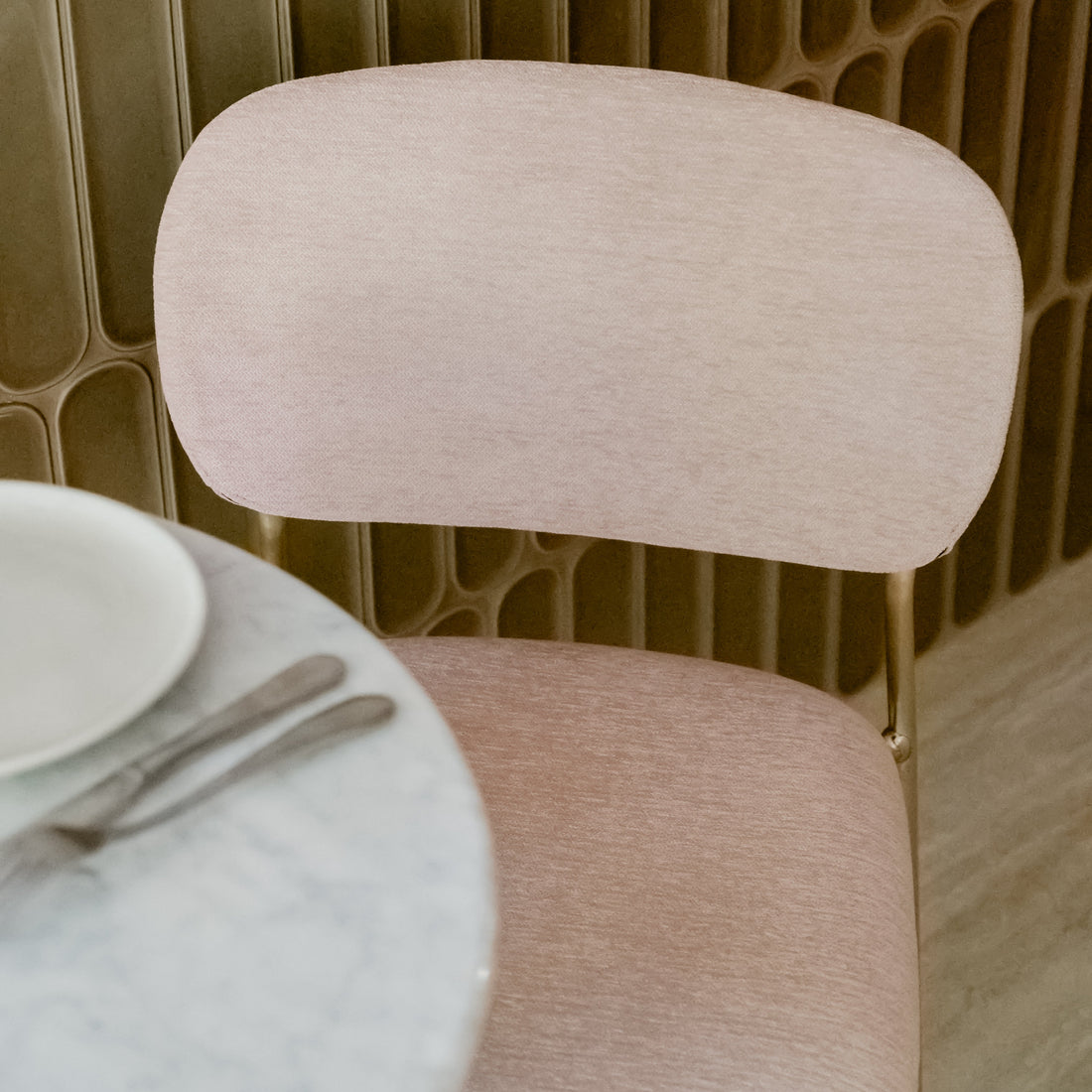 light pink chair next to a round table with a textured wall in the background