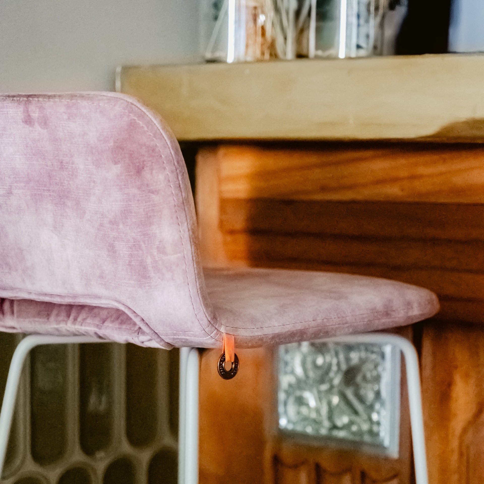 Pink velvet chair with white legs against a wooden wall.