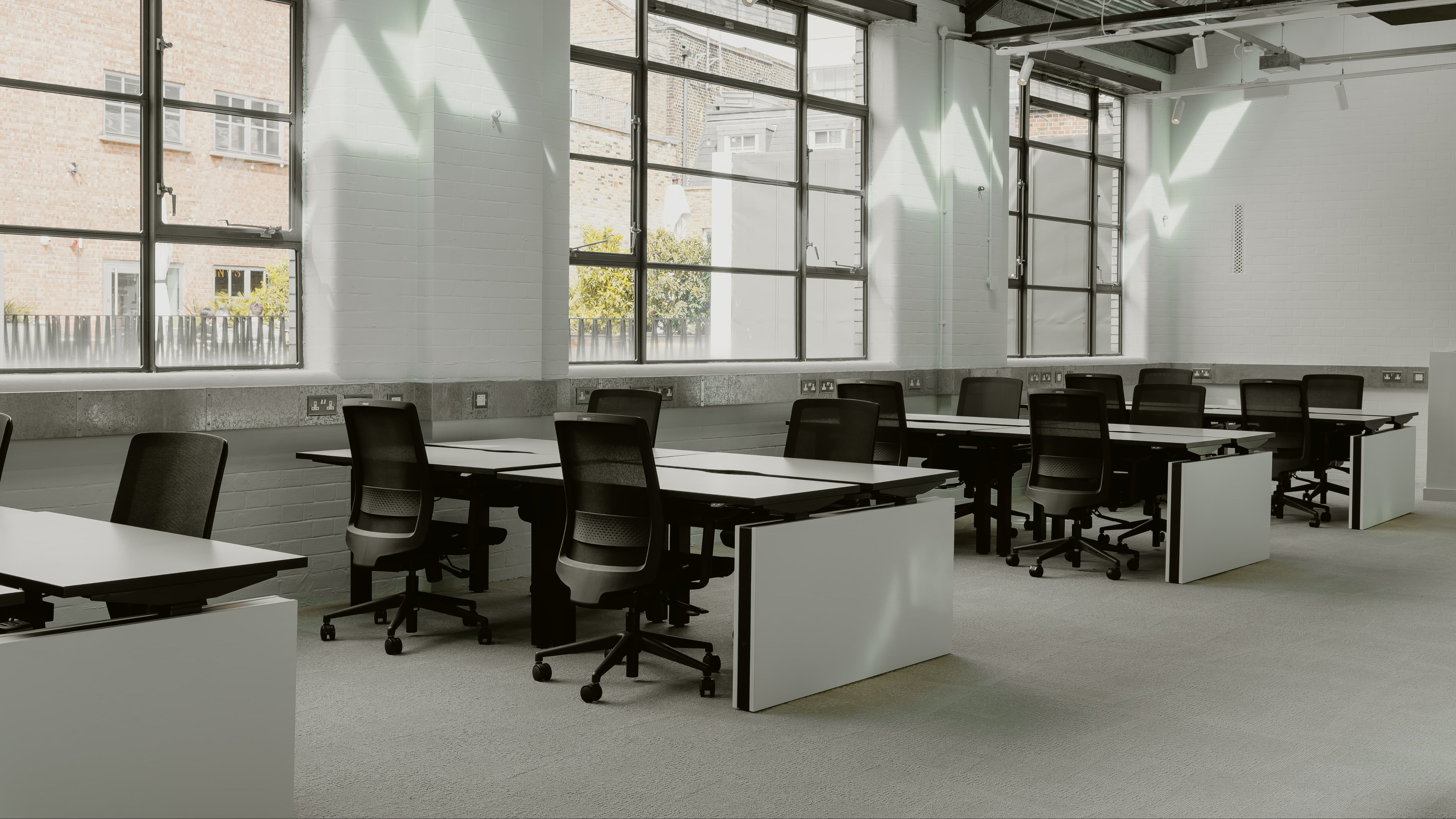 Modern office space with large windows, desks, and chairs.