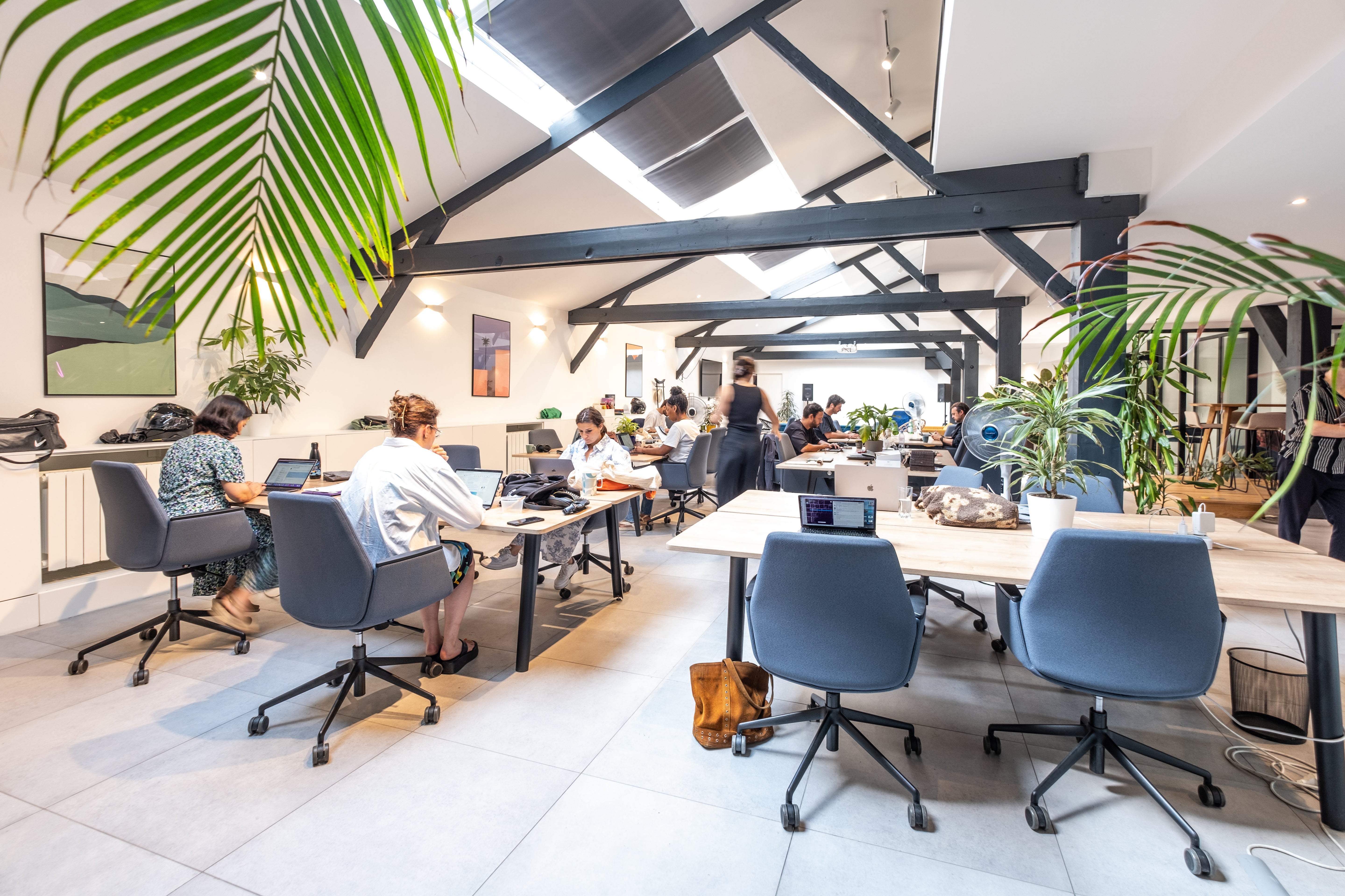 Modern office space with people working at desks, plants, and large windows.