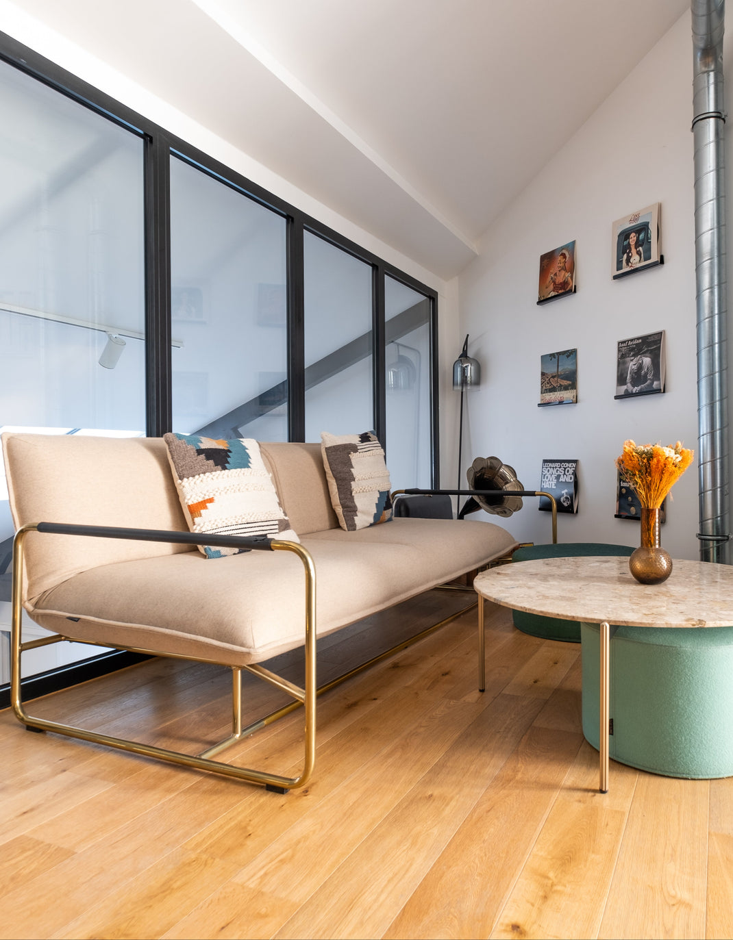 Modern living room with a beige sofa, green ottoman, and wall art.